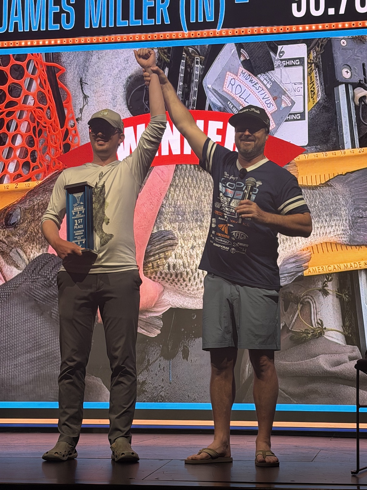 Two men standing on stage. One is holding a trophy