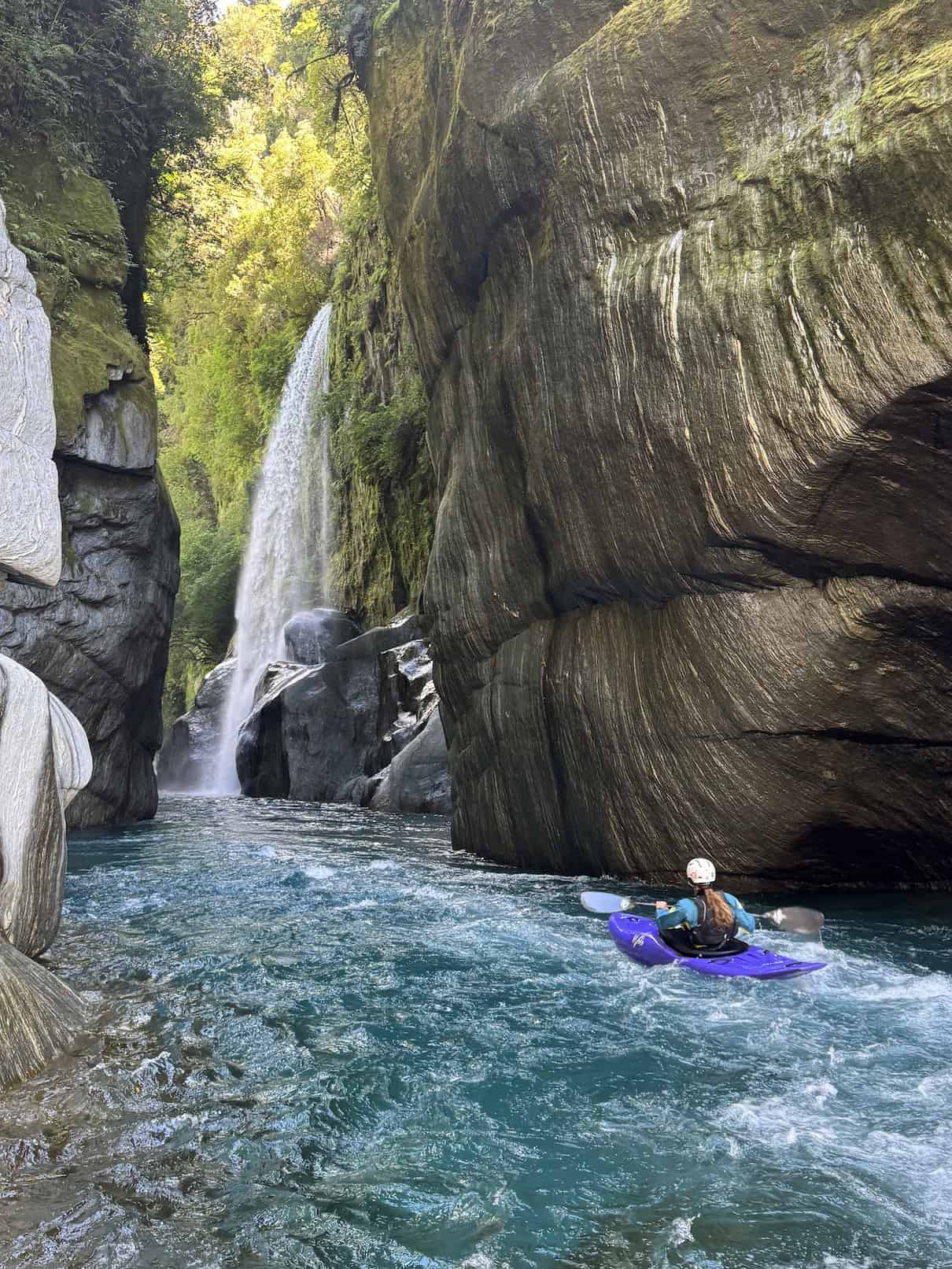 Woman paddling purple whitewater kayak through canyon with waterfall ahead