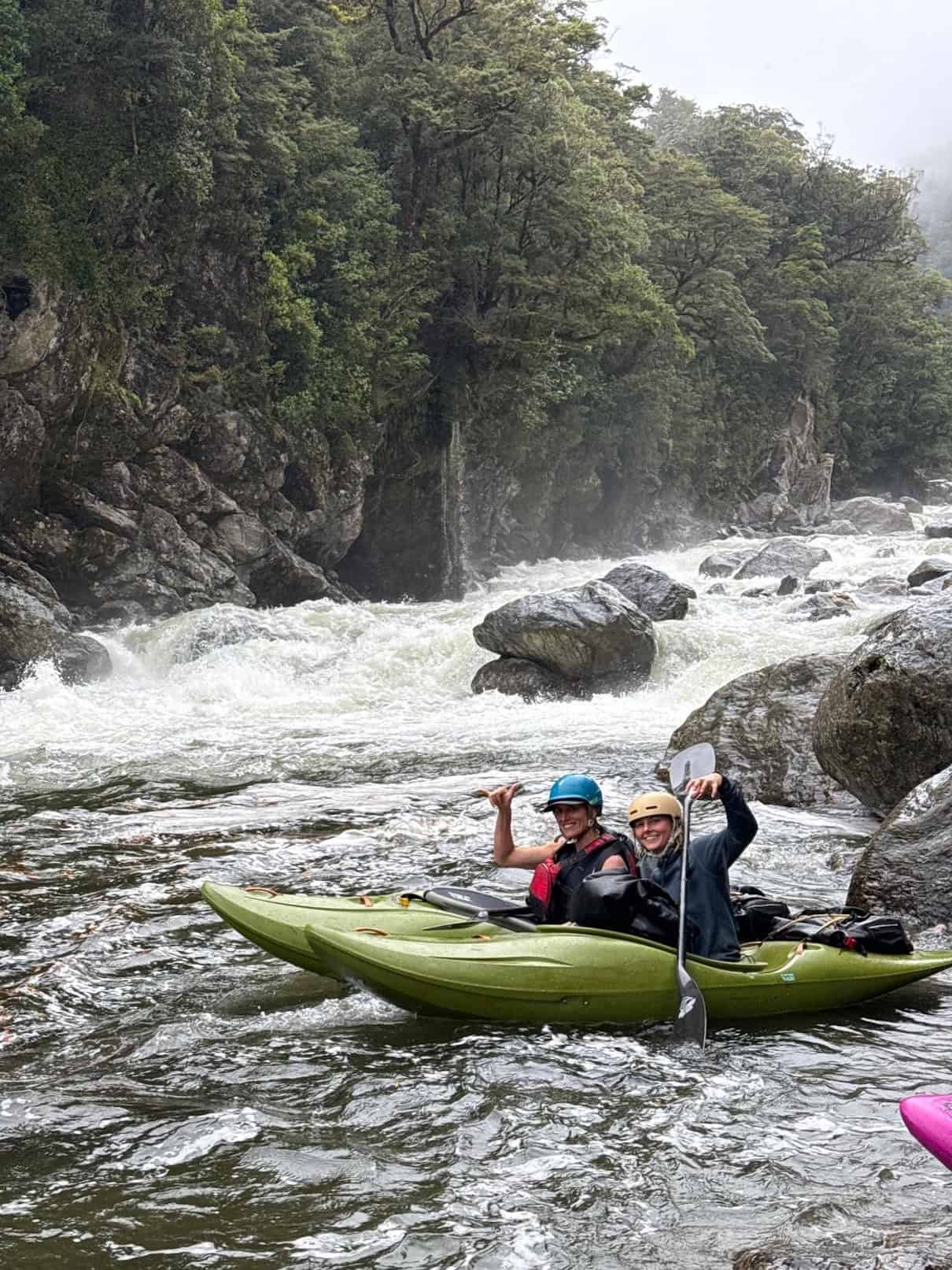 Two women in whitewater kayaks on river with rapids in background
