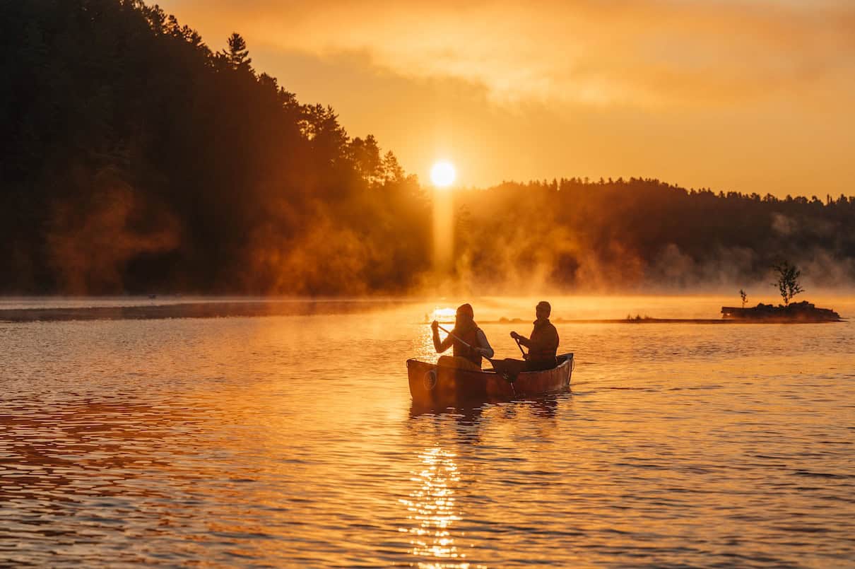Two people paddling canoe on lake at sunrise or sunset.
