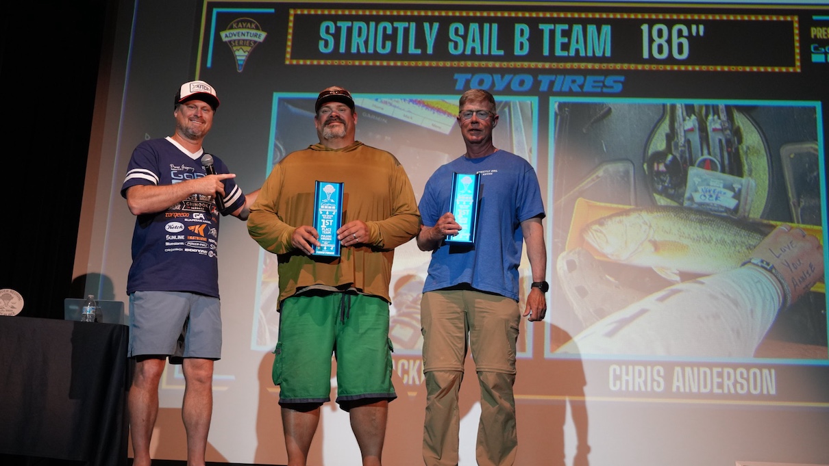 Three men on stage, two holding trophies