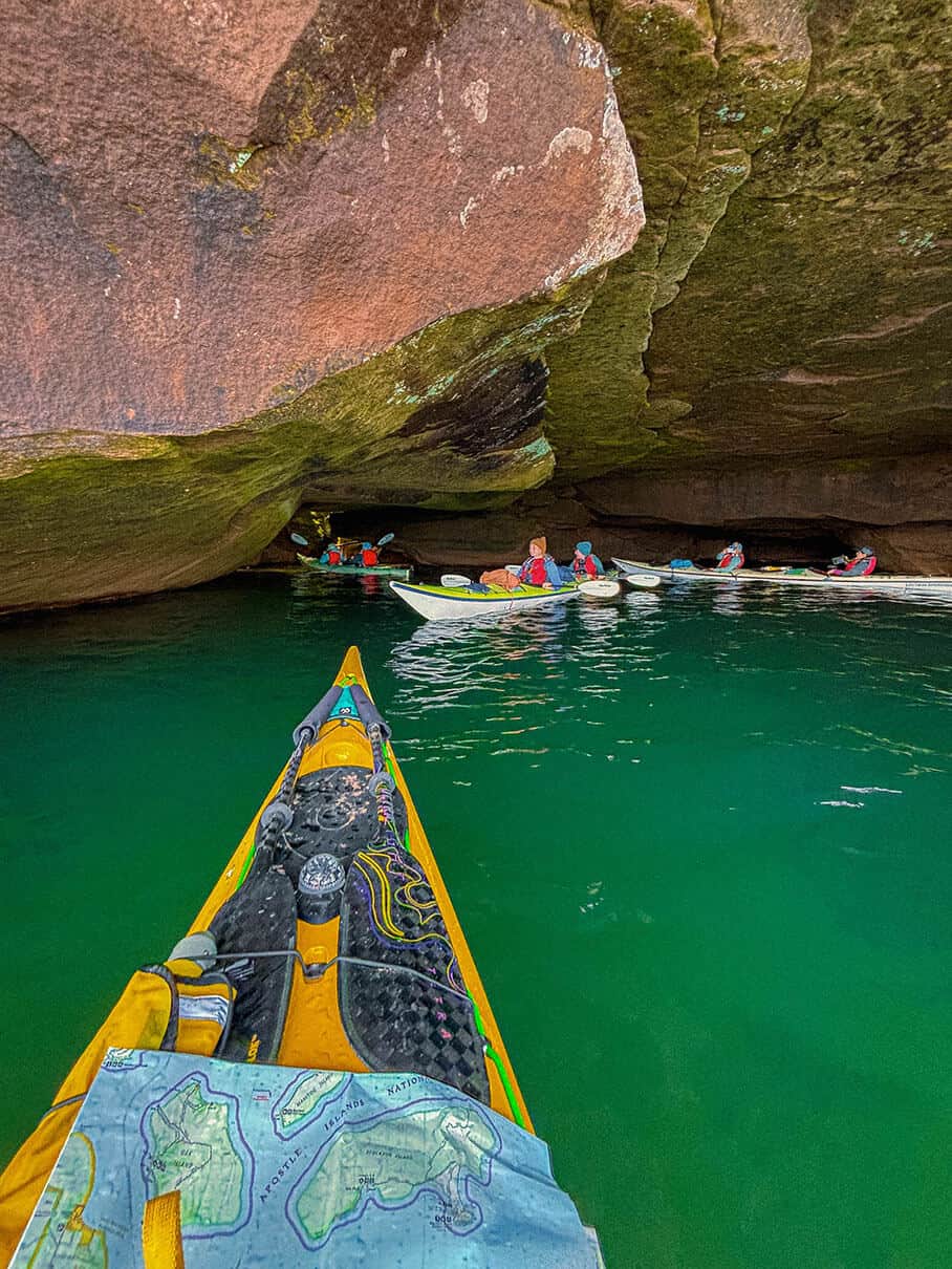 Maddy Marquardt looks at a map while women she is guiding paddle close to shoreline cliffs