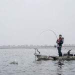 Lobster Rolling Through Maine man stands and fishes from a kayak during rainy weather in Maine