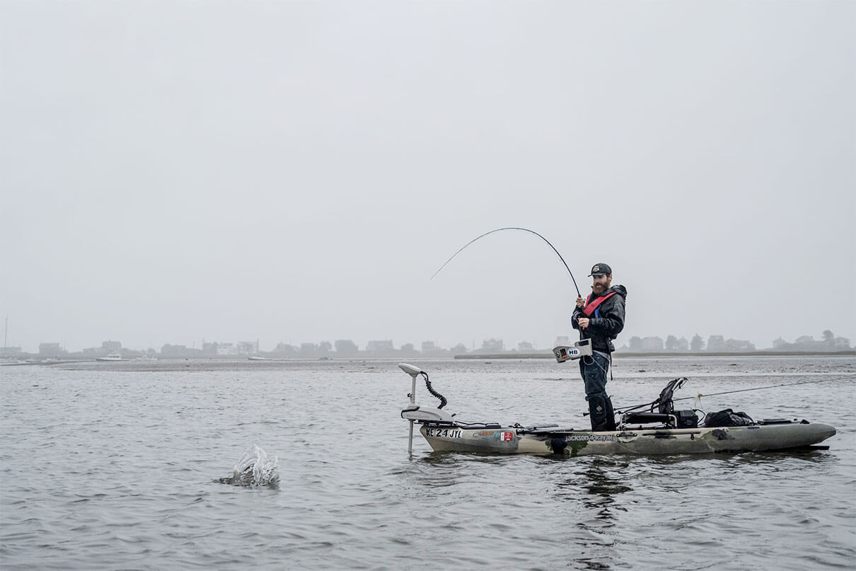man stands and fishes from a kayak during rainy weather in Maine