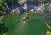 What’s In Editor Maddy Marquardt’s Sea Kayak Day Trip Guiding Kit Paddling Magazine Editor Maddy Marquardt in her sea kayak on a trip with vivid green water, rocks and surrounding foliage in the foreground