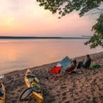 Join Our Upcoming Webinar: How to Get Your Dream Girls’ Paddling Trip Out Of The Group Chat women sit on camp chairs at sunset at a campsite during their girls paddling trip