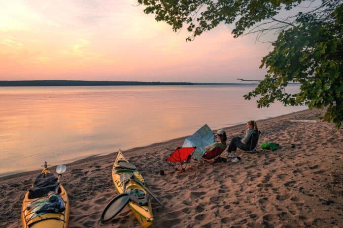 women sit on camp chairs at sunset at a campsite during their girls paddling trip