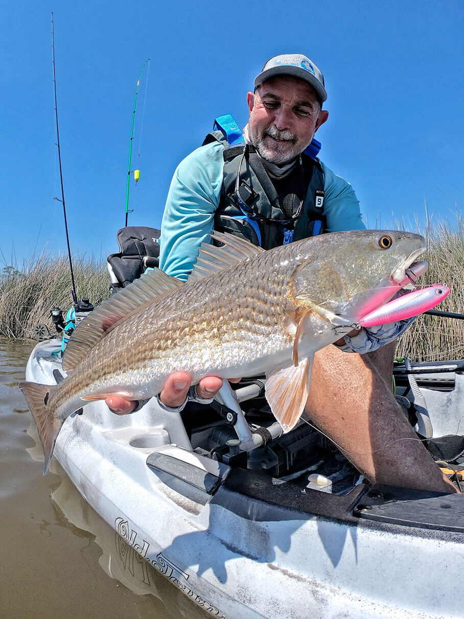 kayak angler holds up a redfish caught with topwater lure