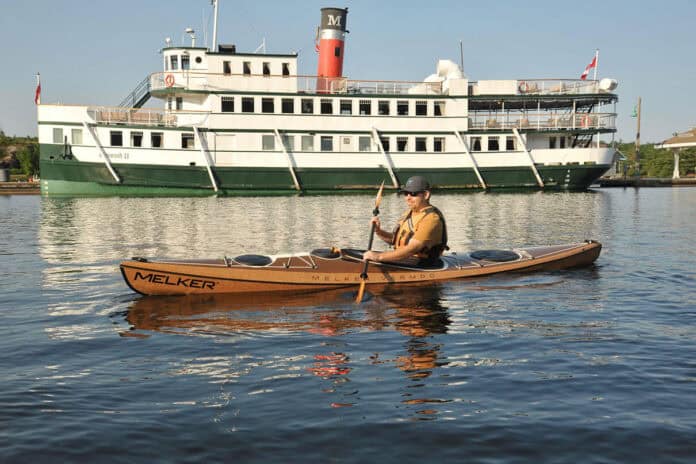 man paddling Melker’s Värmdö kayak with a riverboat in the background