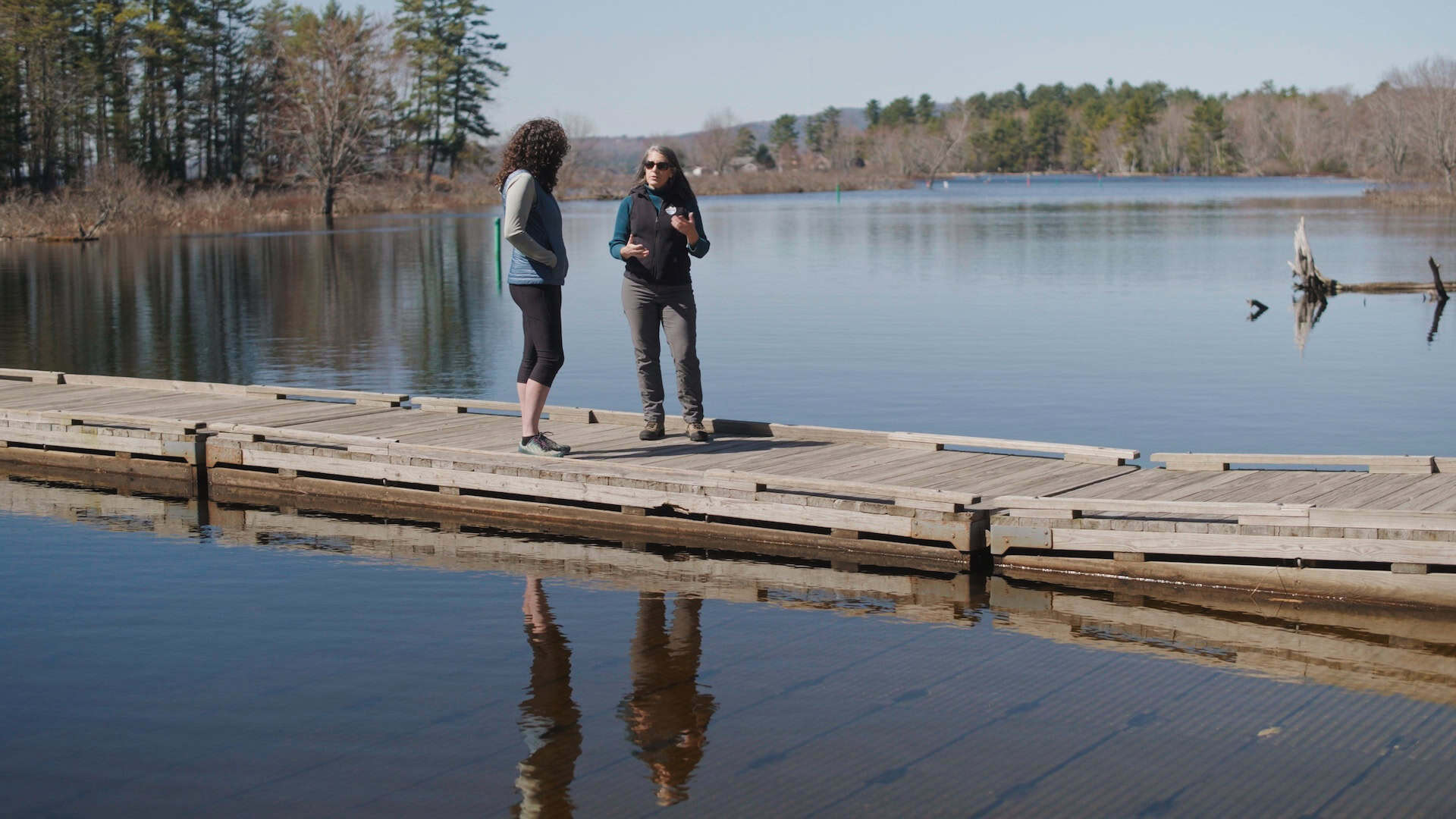 Two women stand on dock on lake