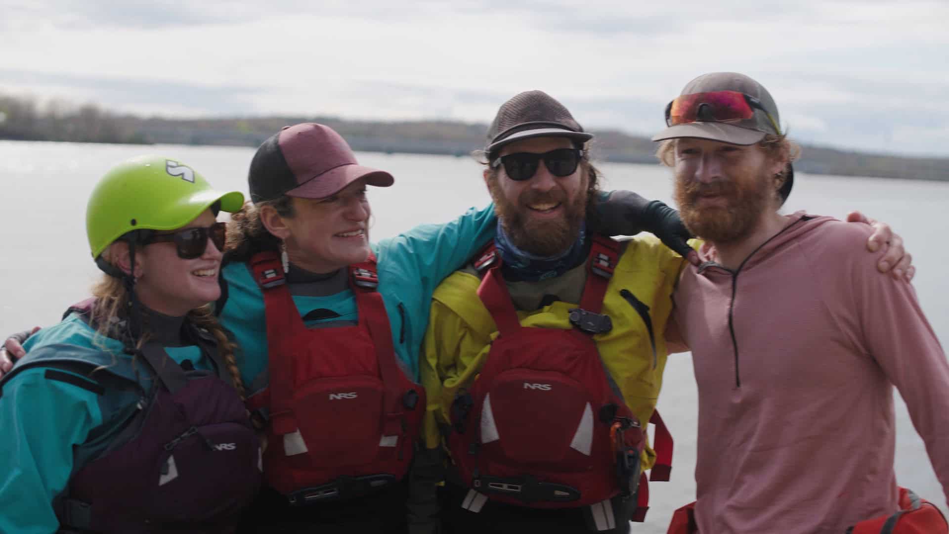 Four paddlers in PFDs stand on shore