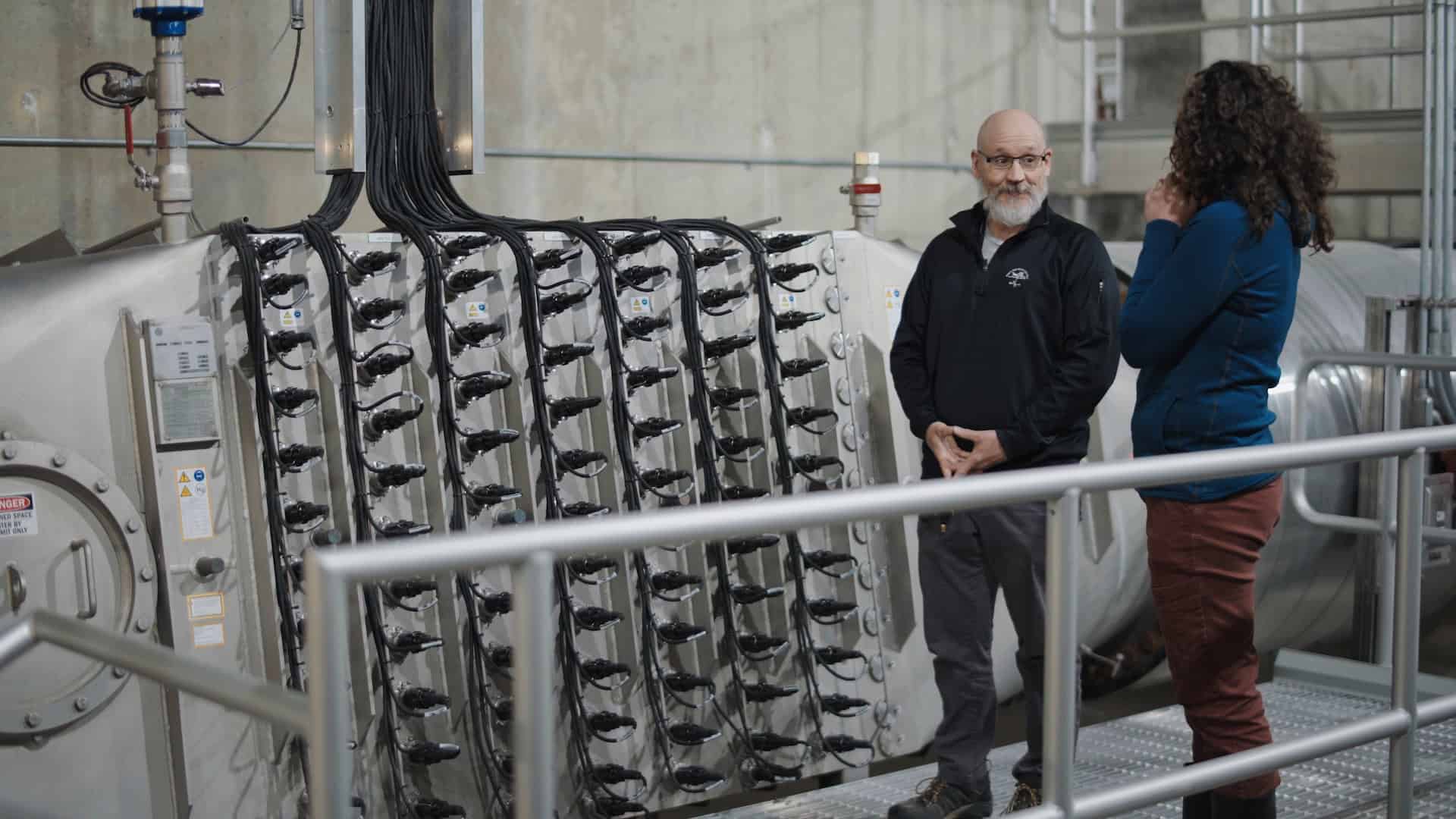 Man and woman stand beside machine in water treatment facility
