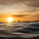 Why Survival Stories Make Us Better Paddlers two people paddle on swells at dusk