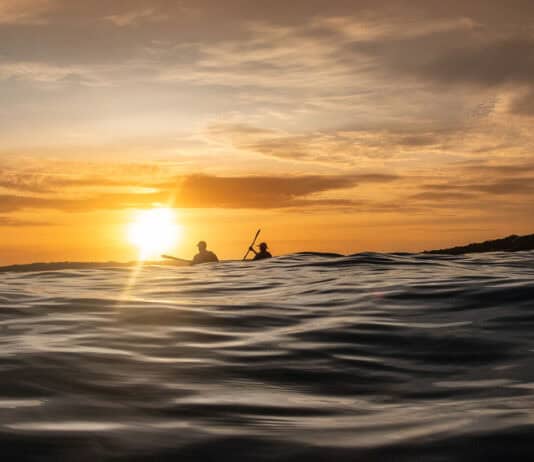 Why Survival Stories Make Us Better Paddlers two people paddle on swells at dusk