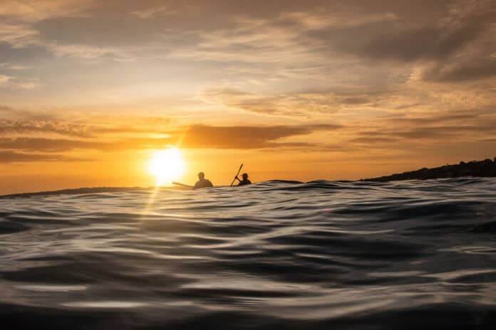 two people paddle on swells at dusk