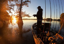 man stands and fishes from kayak at dawn