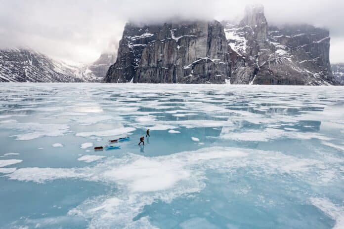 Two people on ice pulling kayaks with mountain in background