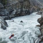 Big Water Theory: Inside The Best Whitewater Film Of 2026 Person in red whitewater kayak going down big rapid with massive boulders and rocky banks