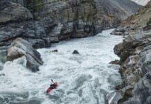 Big Water Theory: Inside The Best Whitewater Film Of 2026 Person in red whitewater kayak going down big rapid with massive boulders and rocky banks