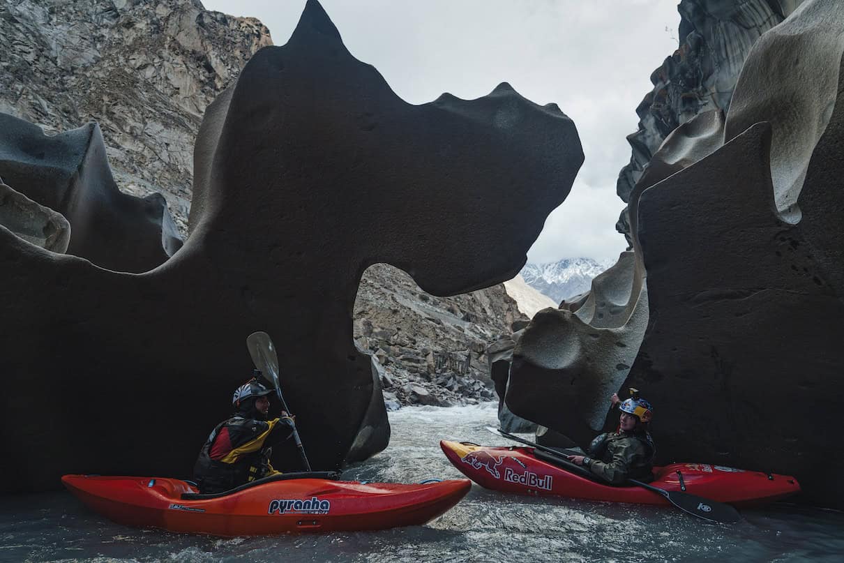 Two people in red whitewater kayaks on river in front of two weird rock formations