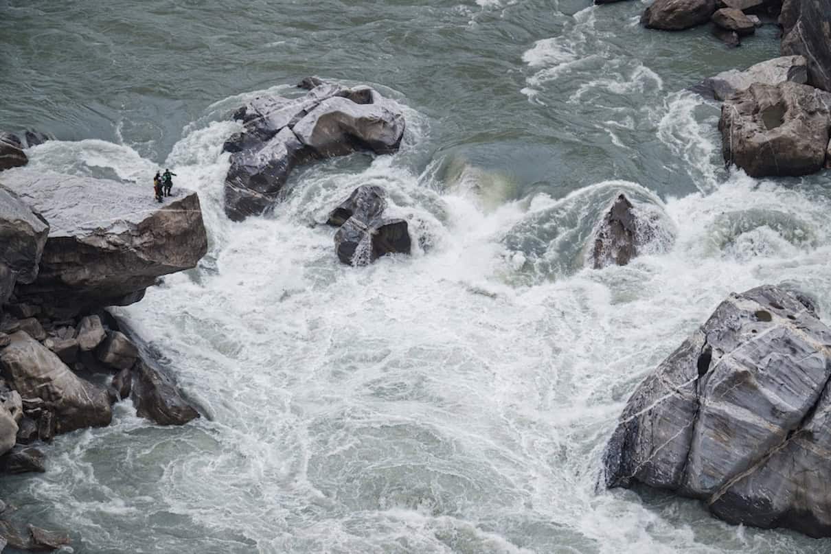 Two people standing on rock overlooking big rapid on river