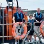 Eight-Year-Old Helps Save Grandfather After Kayak Capsizes boy stands on boat with father and grandfather
