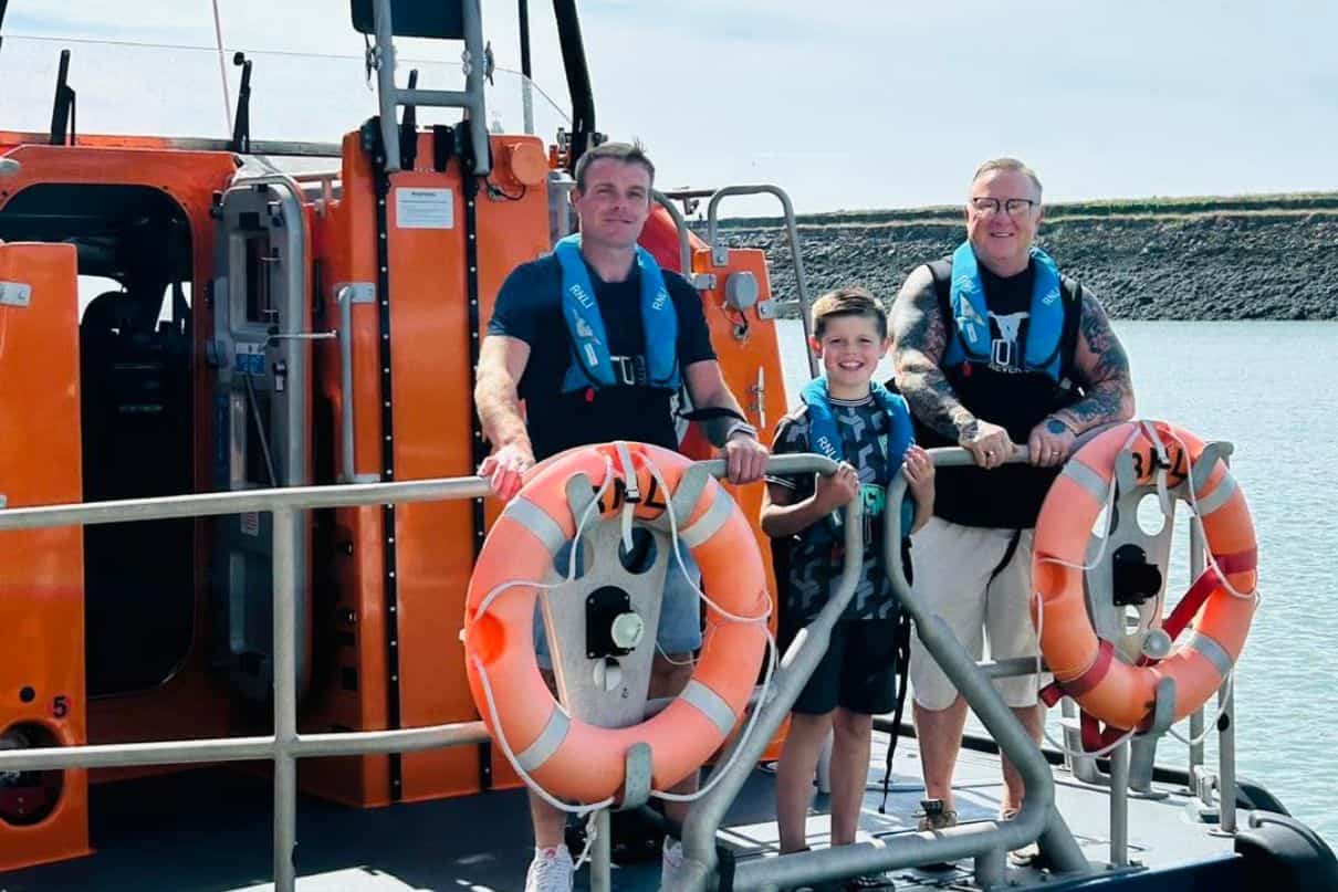 boy stands on boat with father and grandfather