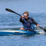 “In The U.S., I Train Alongside The World’s Best Athletes Every Day” Man in sprint kayak on lake.