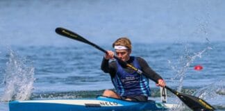 “In The U.S., I Train Alongside The World’s Best Athletes Every Day” Man in sprint kayak on lake.