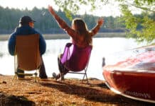 Best Camp Chairs For 2026 Two people sitting in camp chairs near a lake with canoe in foreground.