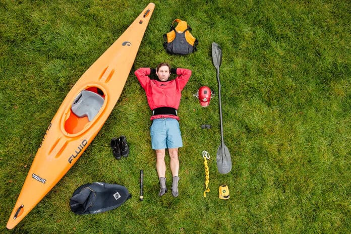 Paddling Magazine Editor Joe Potoczak lays on grass surrounded by his river running gear selections