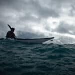 The Less You Know, The Better You Decide person sea kayaks on swell under dark, cloudy skies