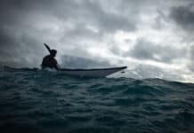 The Less You Know, The Better You Decide person sea kayaks on swell under dark, cloudy skies