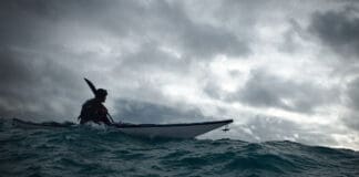 The Less You Know, The Better You Decide person sea kayaks on swell under dark, cloudy skies