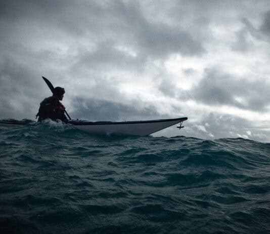 The Less You Know, The Better You Decide person sea kayaks on swell under dark, cloudy skies