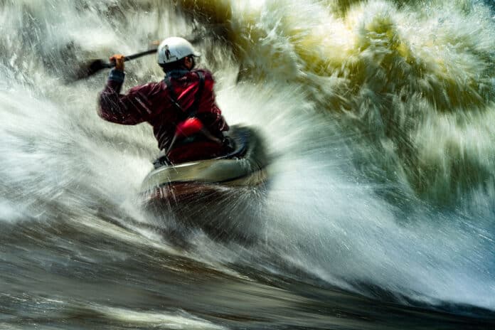 long exposure photo of a man whitewater kayaking in breaking rapids