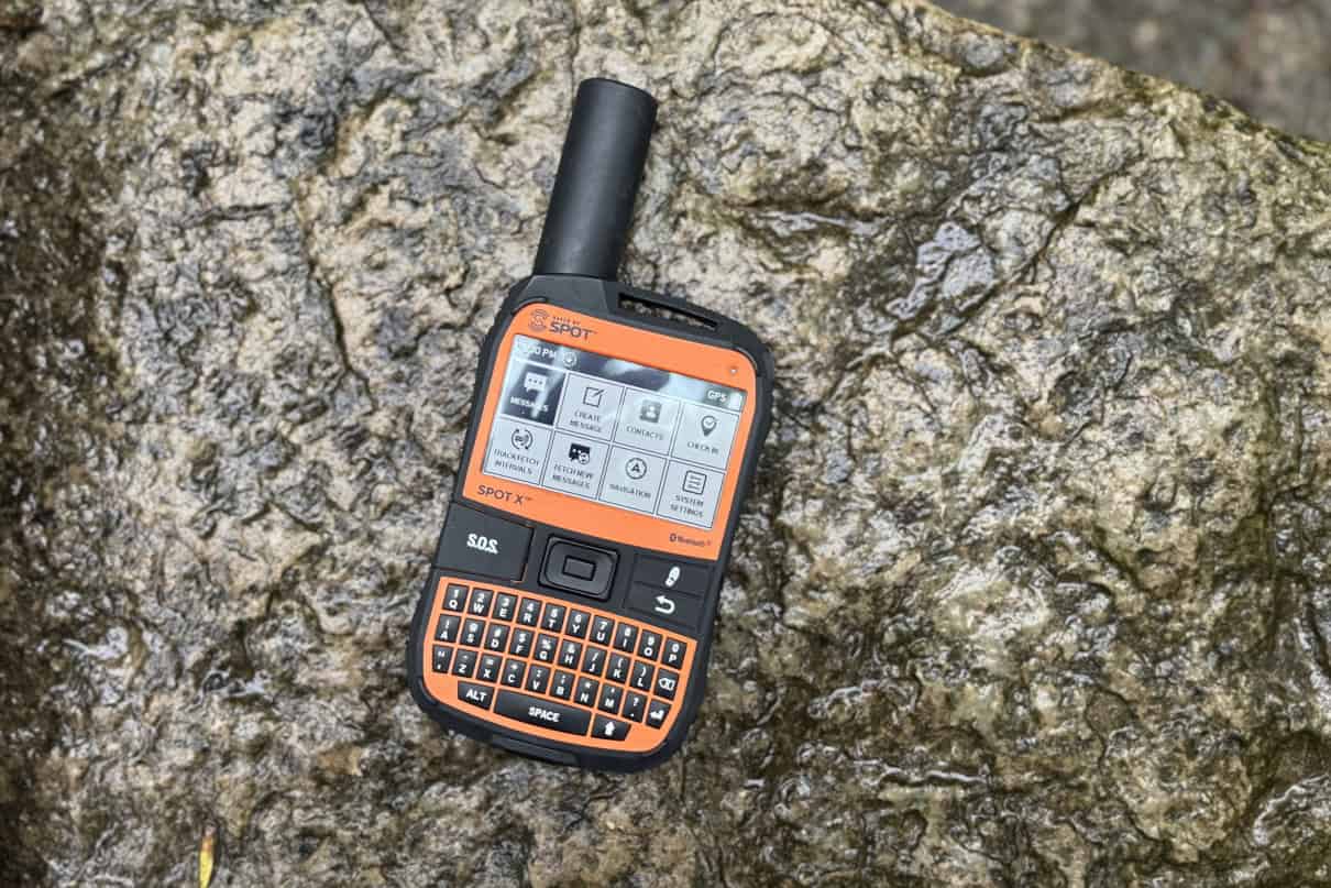 A SPOT X communicator sitting on a wet rock in the outdoors.