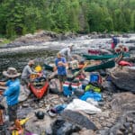 Crowded Canoe Country Isn’t A Crisis a group of people pack gear into canoes along a river