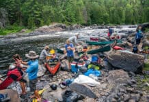 Crowded Canoe Country Isn’t A Crisis a group of people pack gear into canoes along a river