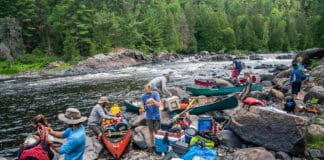 Crowded Canoe Country Isn’t A Crisis a group of people pack gear into canoes along a river