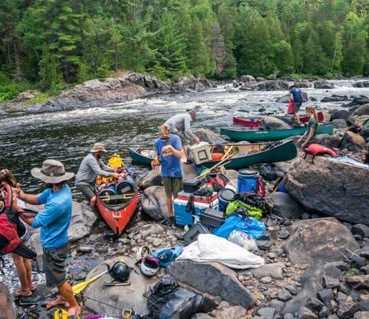 Crowded Canoe Country Isn’t A Crisis a group of people pack gear into canoes along a river