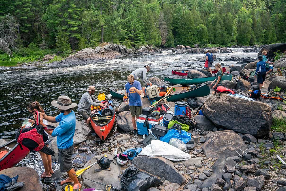 a group of people pack gear into canoes along a river