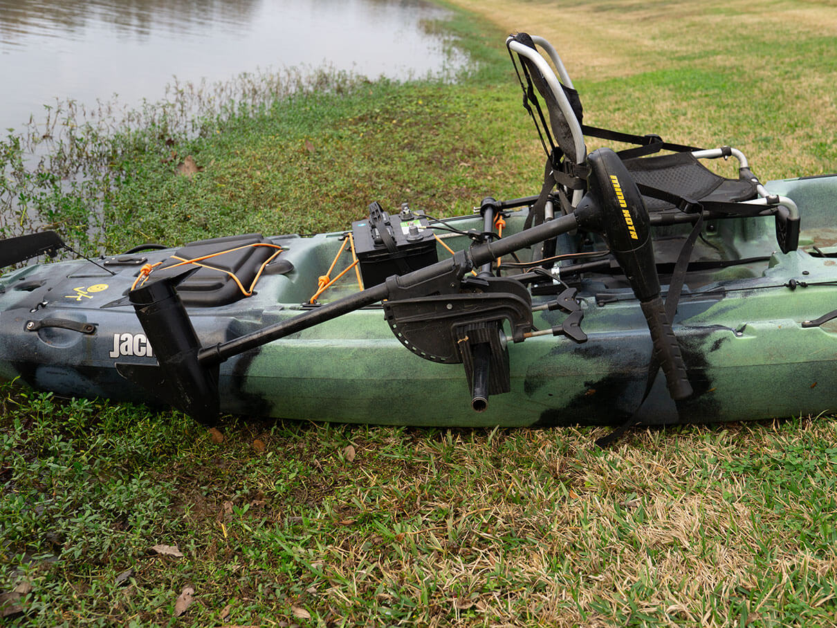 Kayak on grass by the water with DIY motor installed on the starboard side