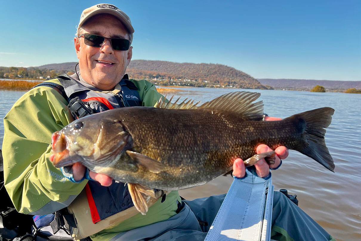 Jeff Little poses with a smallmouth bass caught while kayak fishing on a river