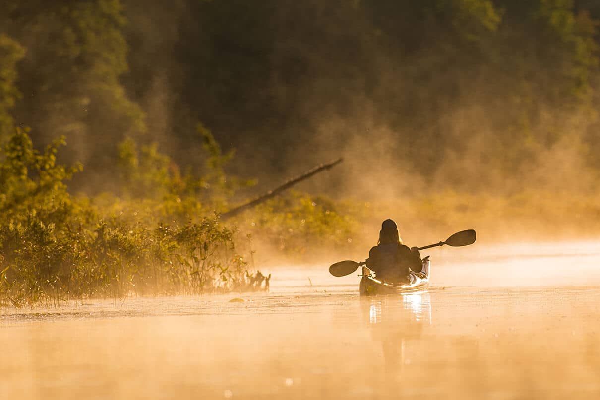 sepia toned photo of someone paddling a kayak in early morning mist